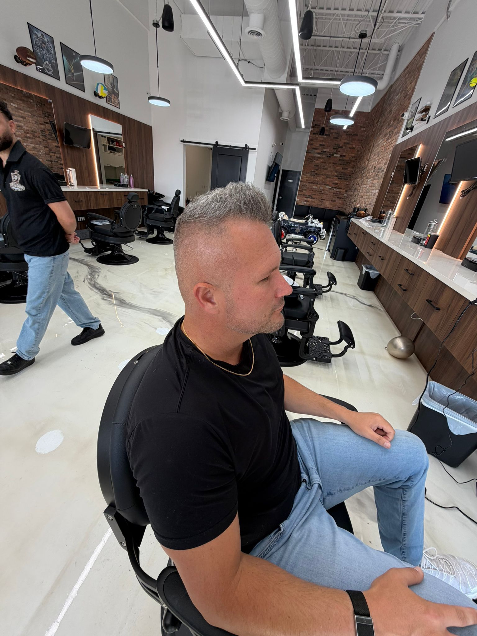 Client with a high and tight cut, grey textured top and skin-faded sides, sitting in a barber chair at New Legend Barbershop in Hamilton