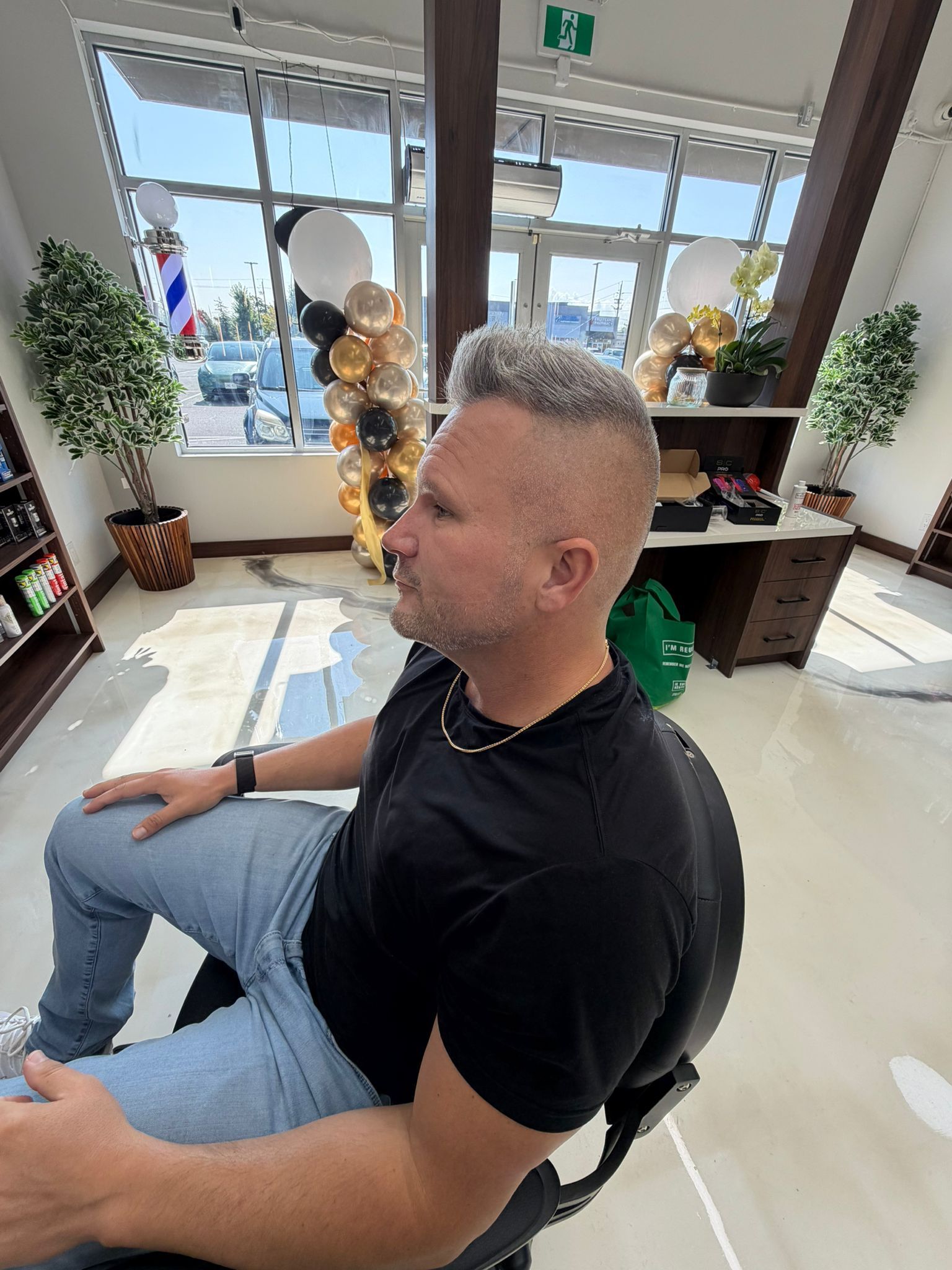 Client with grey hair cut into a high skin fade with a short spiked top, seated in front of a barber pole at New Legend Barbershop in Hamilton