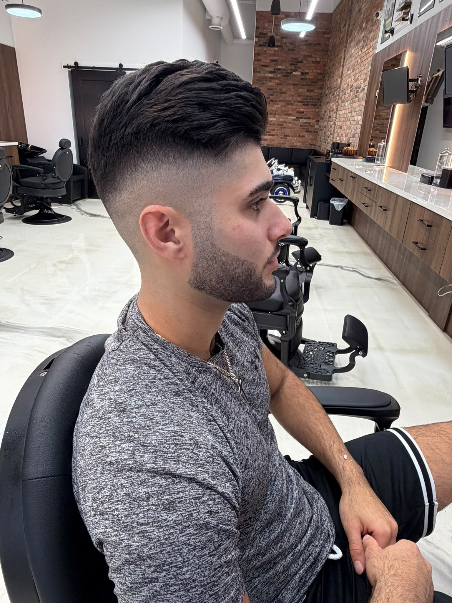 Client with a mid skin fade blending into a faded beard and a textured quiff on top, at New Legend Barbershop in Hamilton