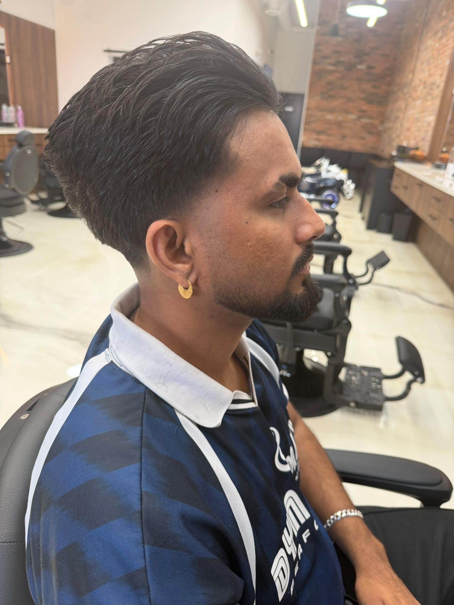 Side profile of a client with long slicked-back hair, a low taper fade around the ear and a trimmed beard, at New Legend Barbershop in Hamilton